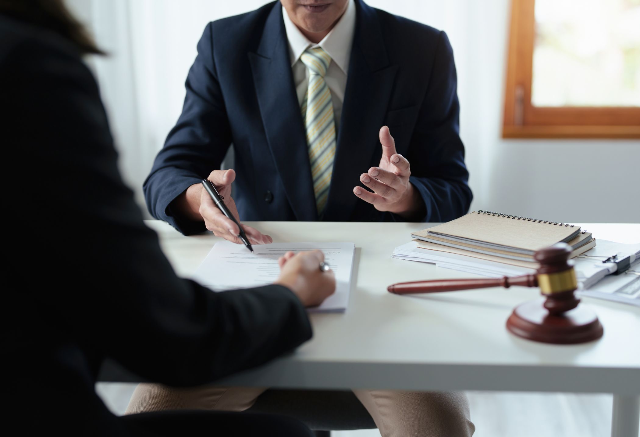 A lawyer gestures while discussing documents with a client at a desk, accompanied by legal papers and a gavel.